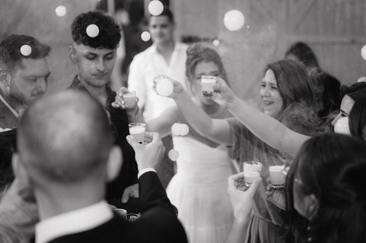 A group raises glasses in celebration at a black and white party photograph with bokeh lights in background.