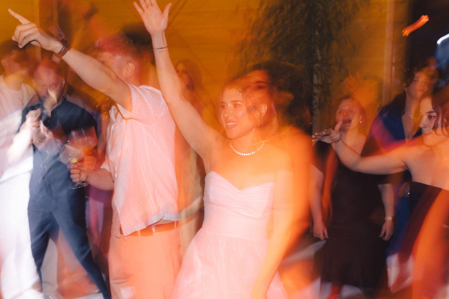 Blurred motion shot of people dancing at a party with orange lighting and energetic movement.