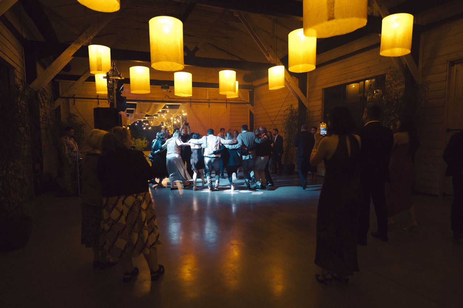 Musicians performing in a dimly lit venue with glowing yellow pendant lights hanging from wooden beams above.