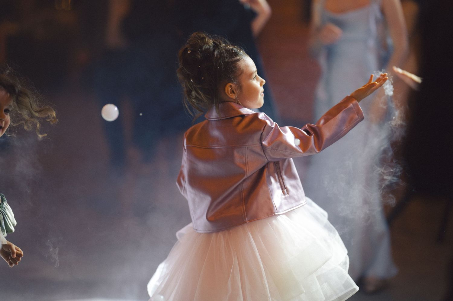A young dancer in a tulle dress performs gracefully on stage amidst atmospheric fog and lighting effects.