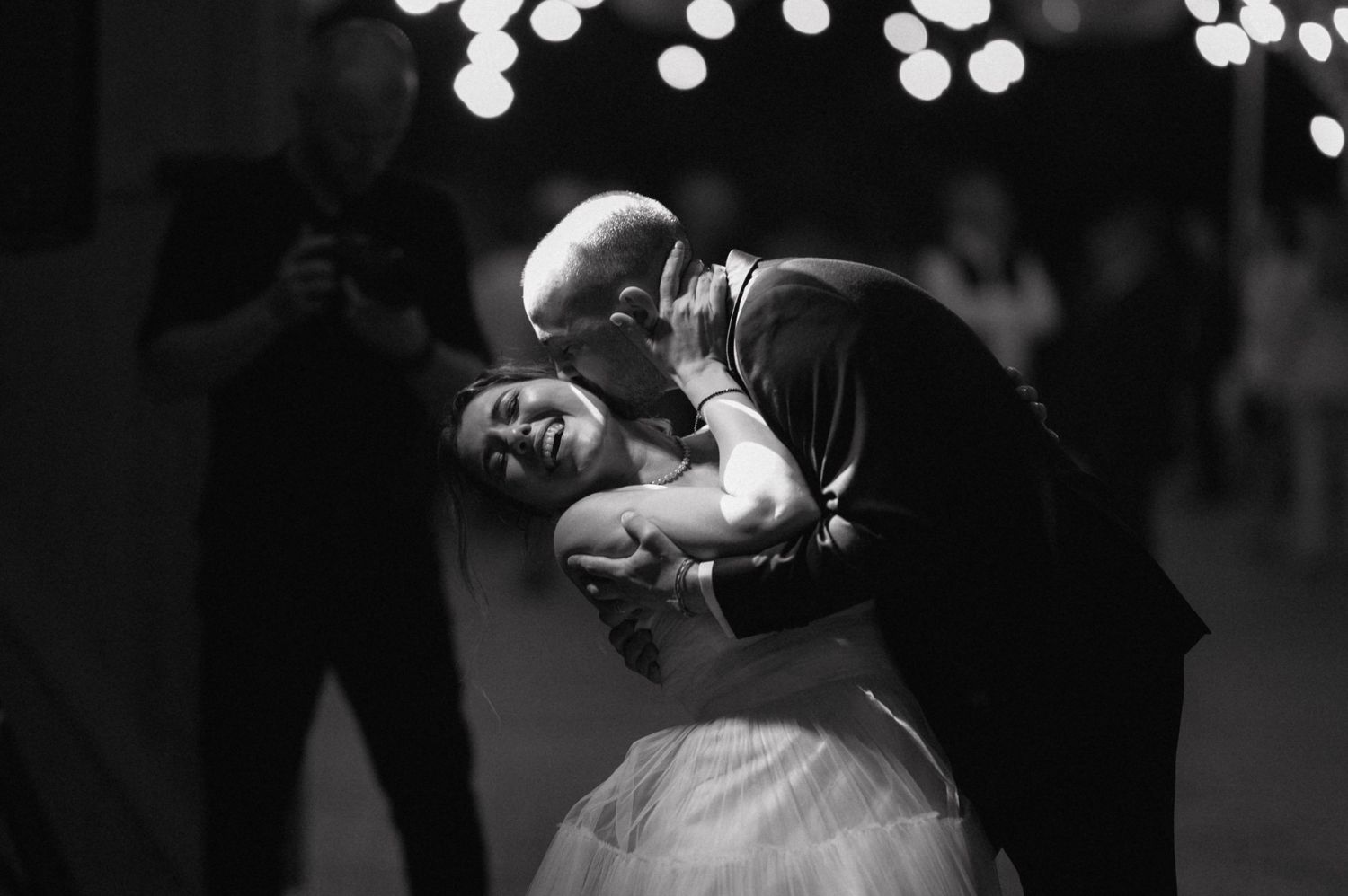 A couple shares an intimate dance moment under twinkling lights during what appears to be a wedding celebration.