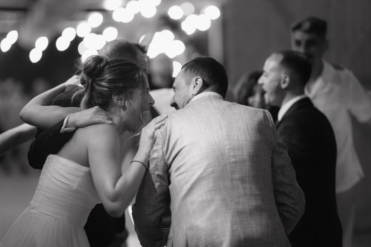 A couple shares an intimate moment while dancing at a wedding reception with blurred lights in the background.