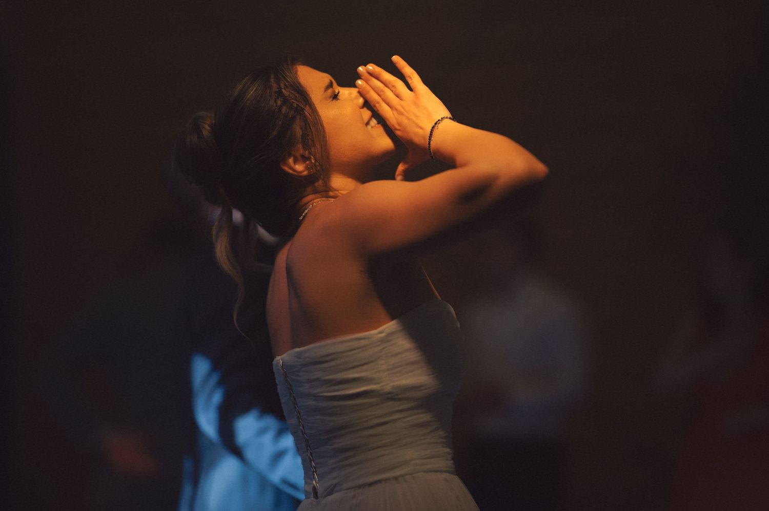 A songwriter in a white dress performs emotionally on a dimly lit stage with dramatic lighting effects.