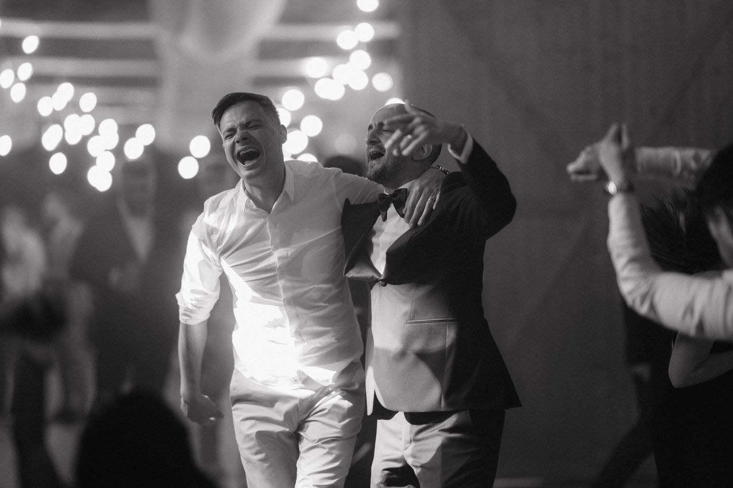 Black and white photo showing people dancing together on a dimly lit dance floor with blurred lights in the background.