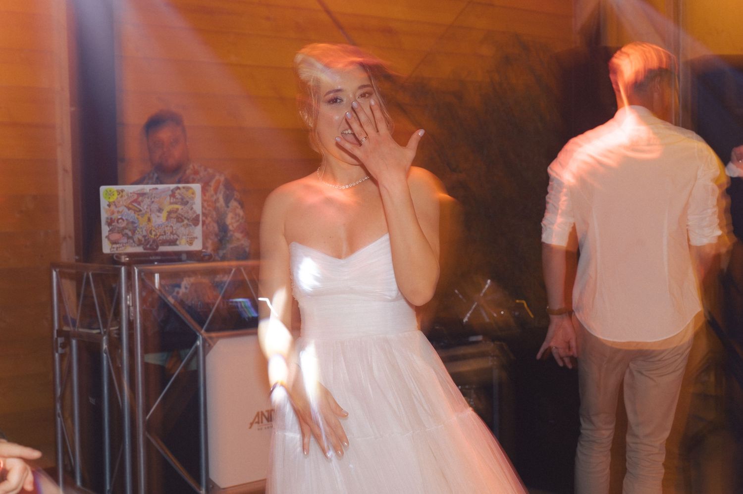 An emotional moment captured at a wedding reception with a bride in a white dress as warm orange lighting fills the space.