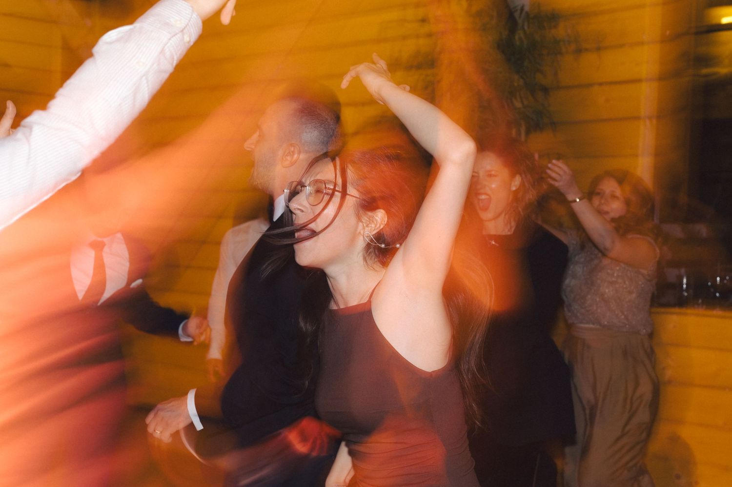 Dancers move energetically in a blurred motion capture against warm lighting at a lively party or club event.