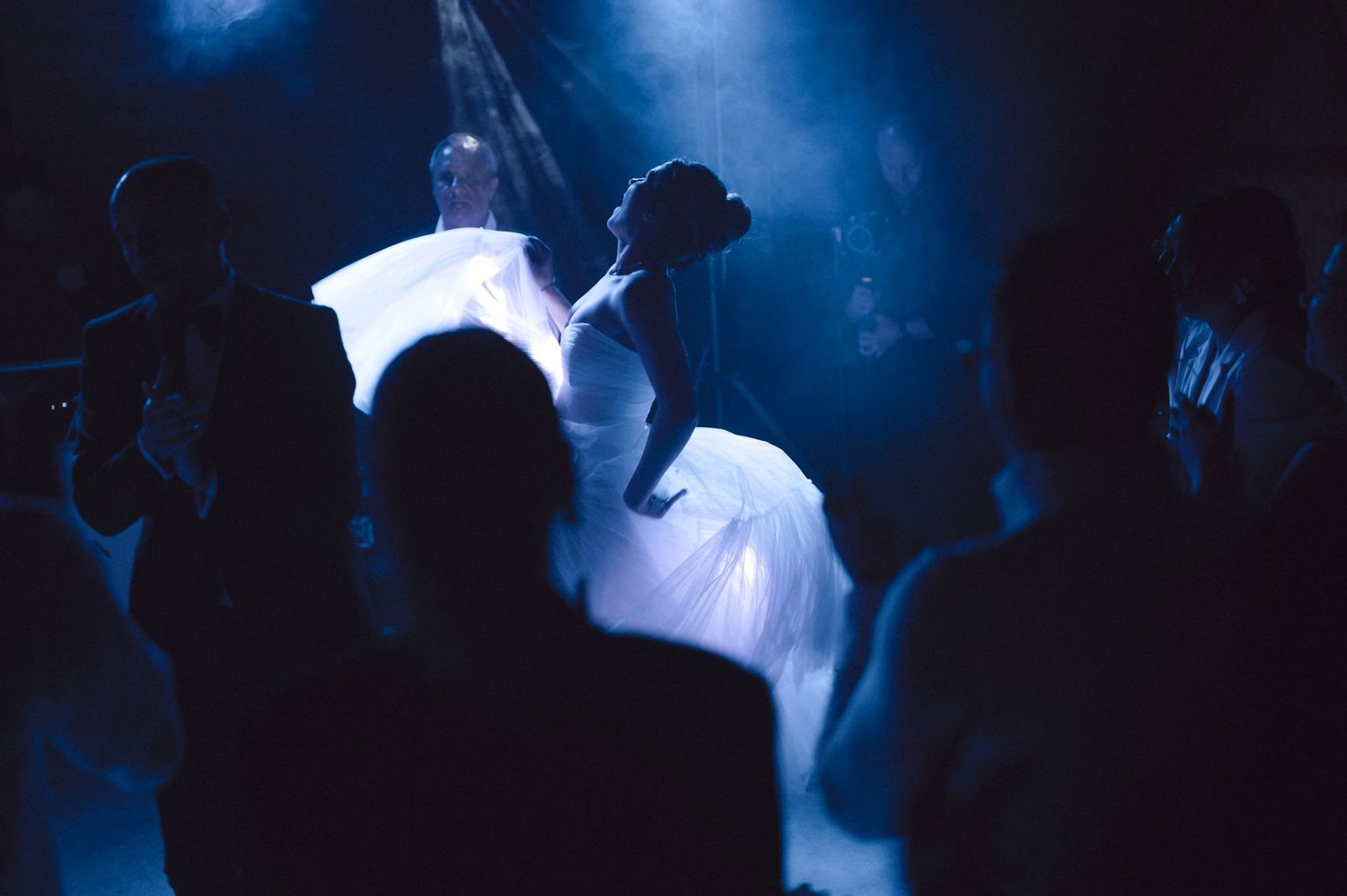 Silhouettes of dancers perform in front of dramatic blue stage lighting.