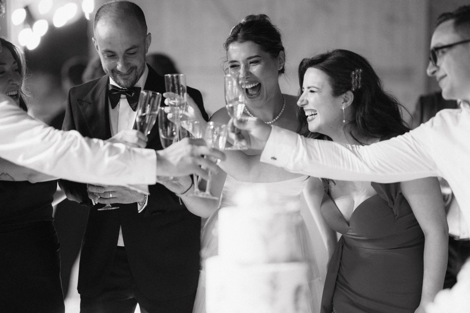 Wedding guests and the bride raise their glasses in a joyful black and white champagne toast at a celebration.