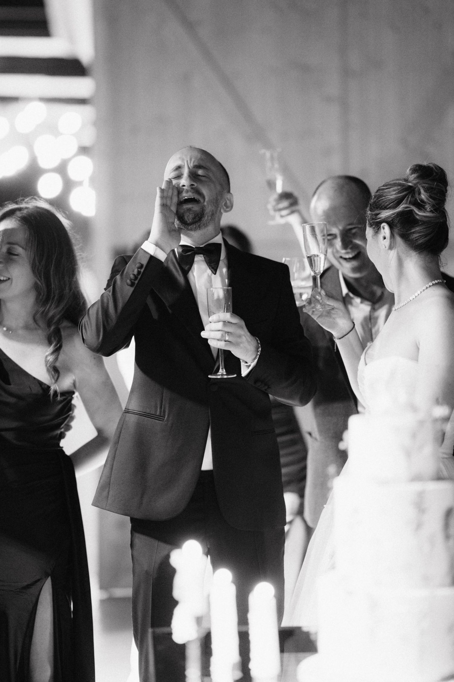 Wedding celebration with guests in formal attire laughing and raising champagne glasses in joyful toast.