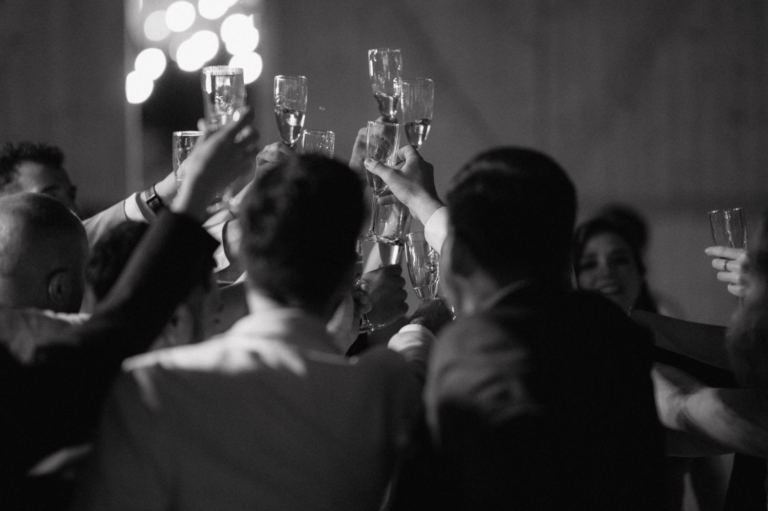 A black and white photograph shows silhouettes of people raising glasses in celebration at what appears to be a party.