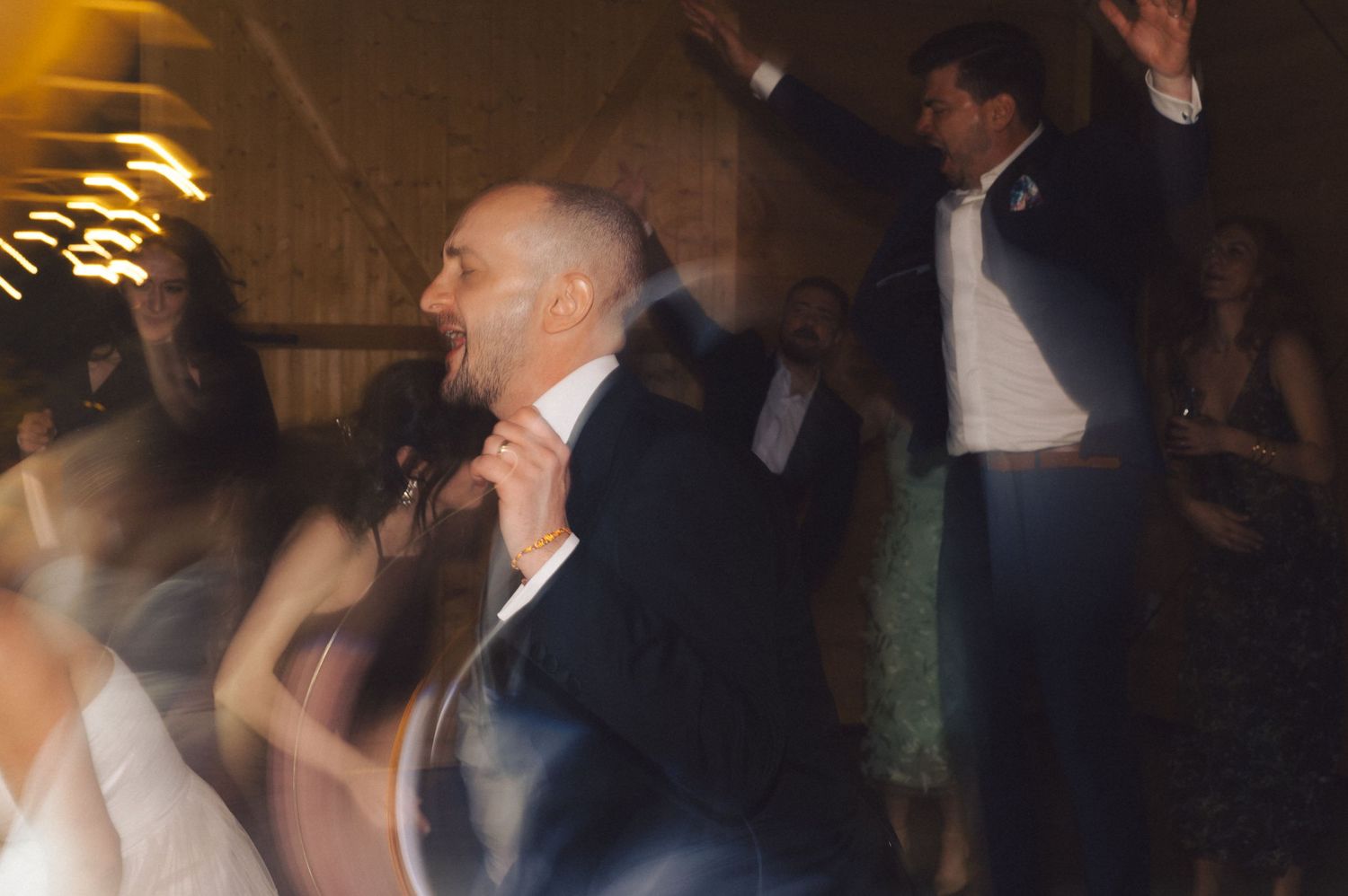 People dancing and celebrating at a dimly lit evening party or reception with warm lighting overhead.