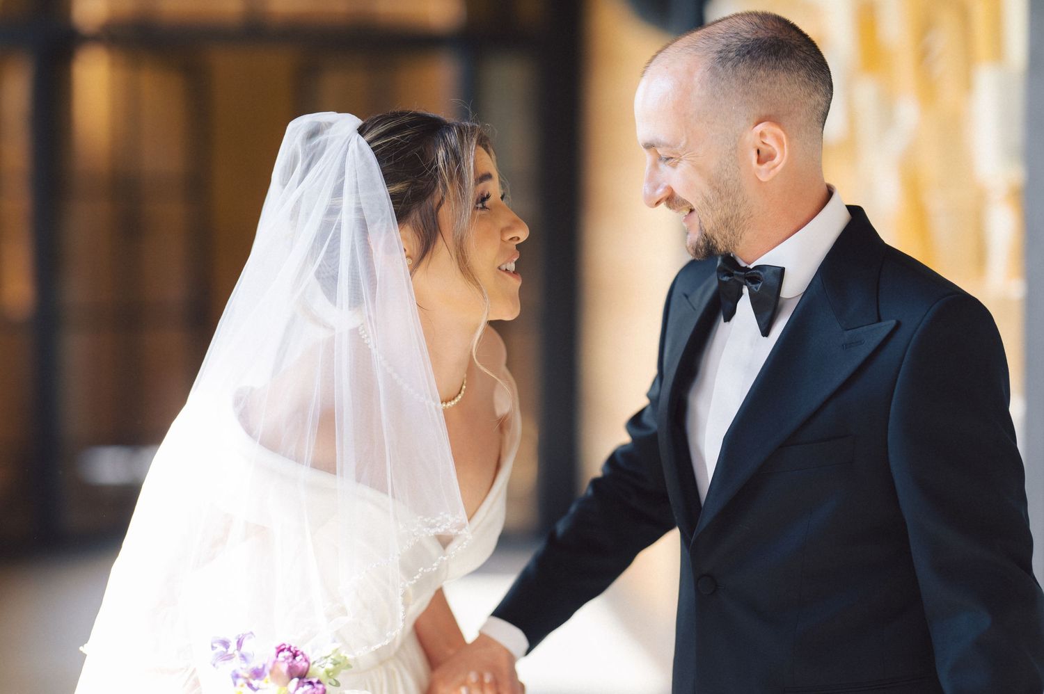 A joyful couple laughs together on their wedding day, with the bride in white and the groom in a classic tuxedo.