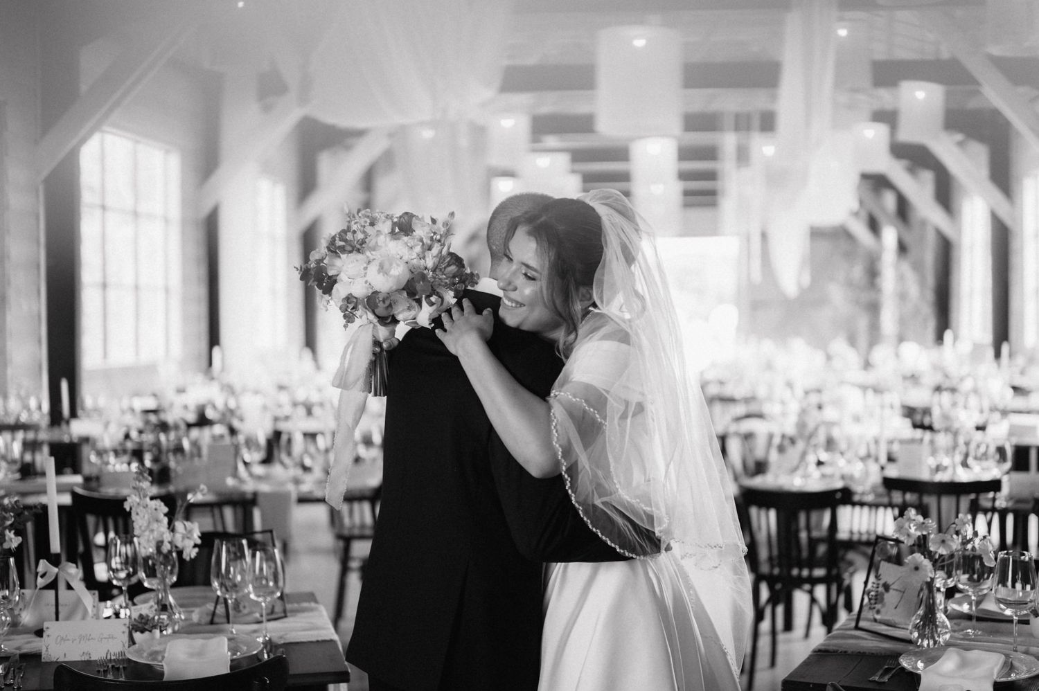 A tender embrace between two people at an elegant wedding reception venue filled with dining tables.
