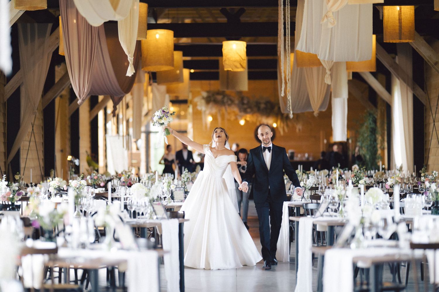 Elegant reception venue with soft draping, warm lighting and formal dining tables set for a wedding celebration.