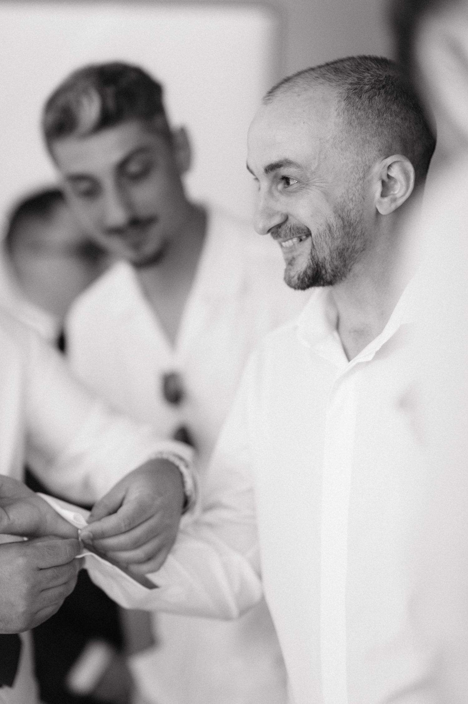 Black and white photograph of two men in white shirts sharing a joyful moment during preparations.