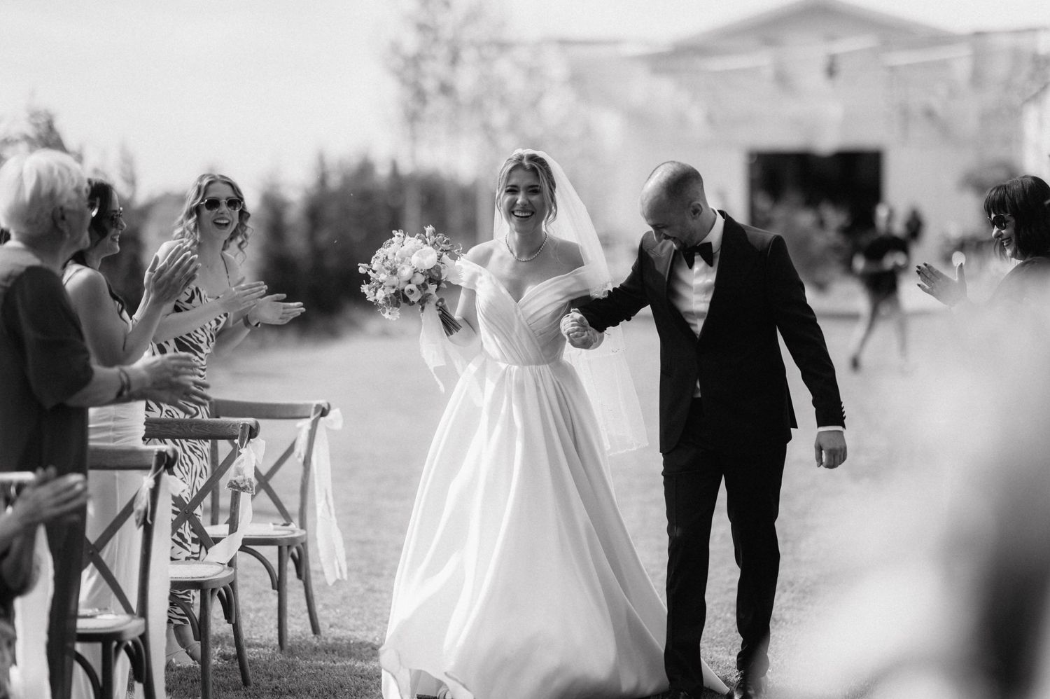 A joyful couple walks down an outdoor aisle while guests shower them with confetti at an elegant garden wedding ceremony.