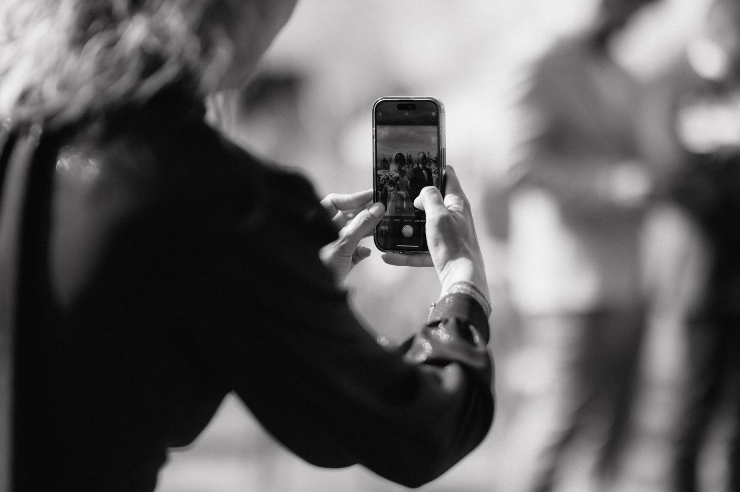 Black and white photo of hands holding smartphone taking a photo in a blurred setting.
