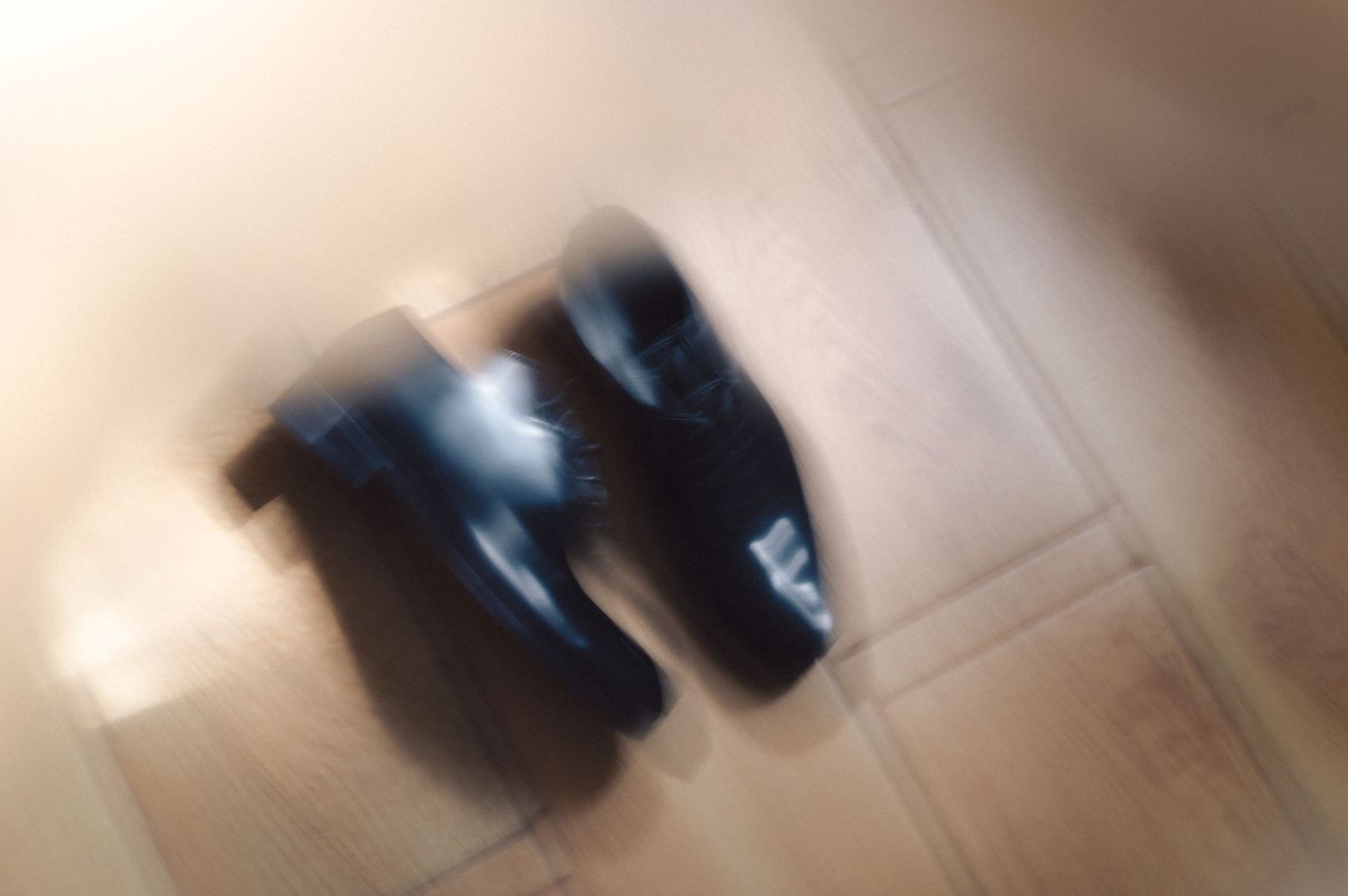 Blurry black shoes or boots on a wooden floor with soft natural lighting.