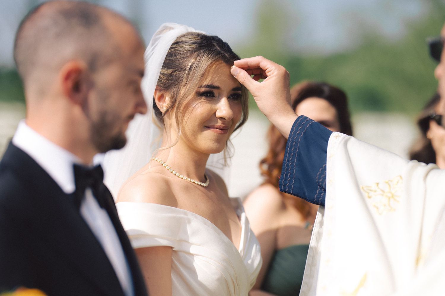 A couple participates in a traditional Catholic wedding ceremony as a priest performs a blessing outdoors.