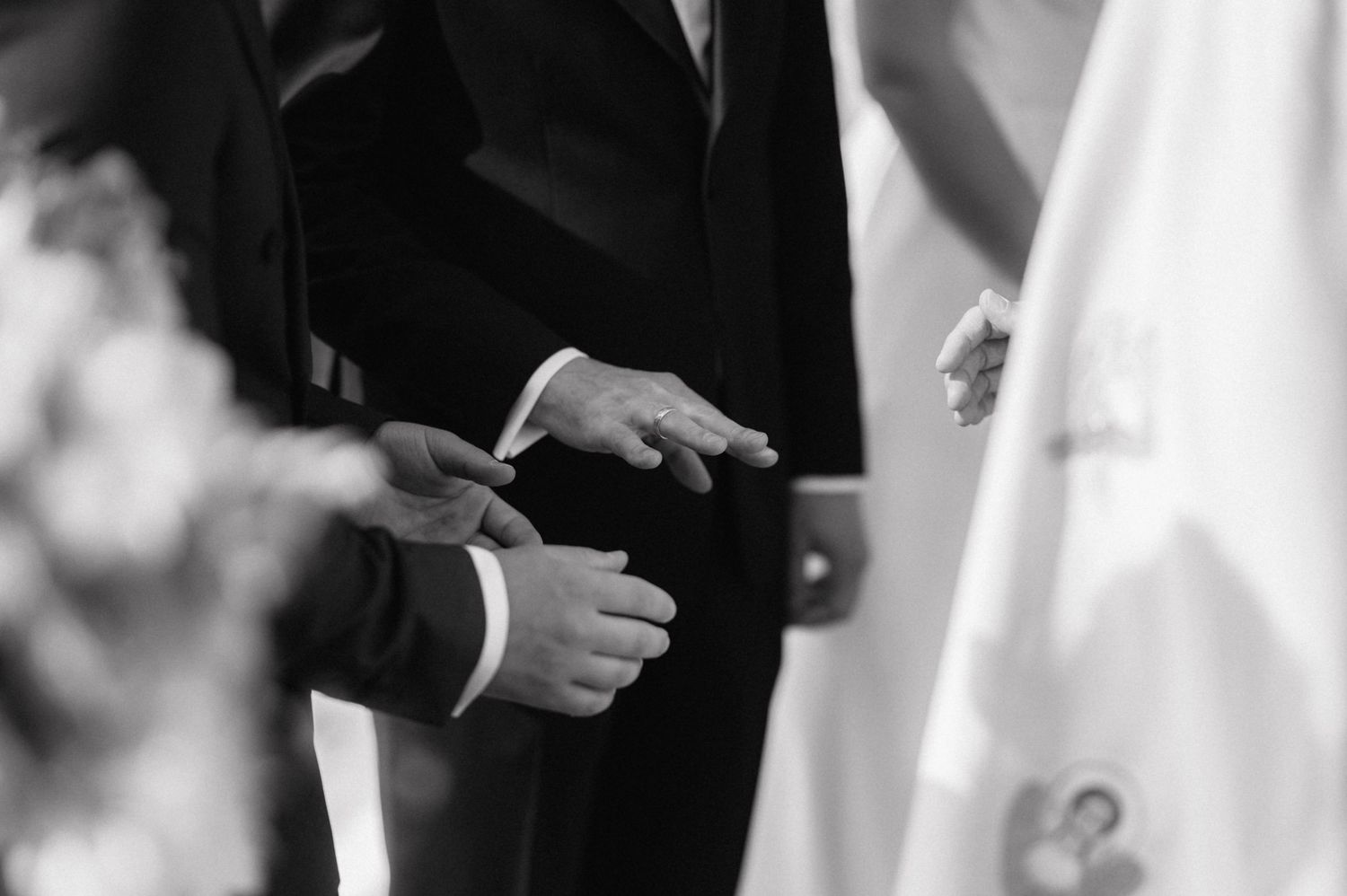 Black and white image of two hands exchanging wedding rings during a marriage ceremony.