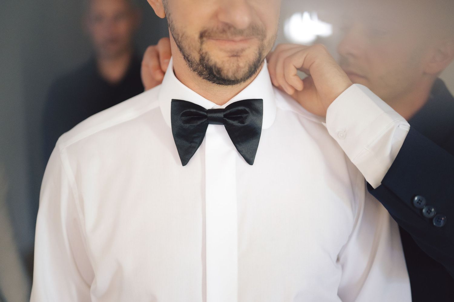 Close-up view of formal attire showing a crisp white dress shirt and black bow tie in elegant lighting.