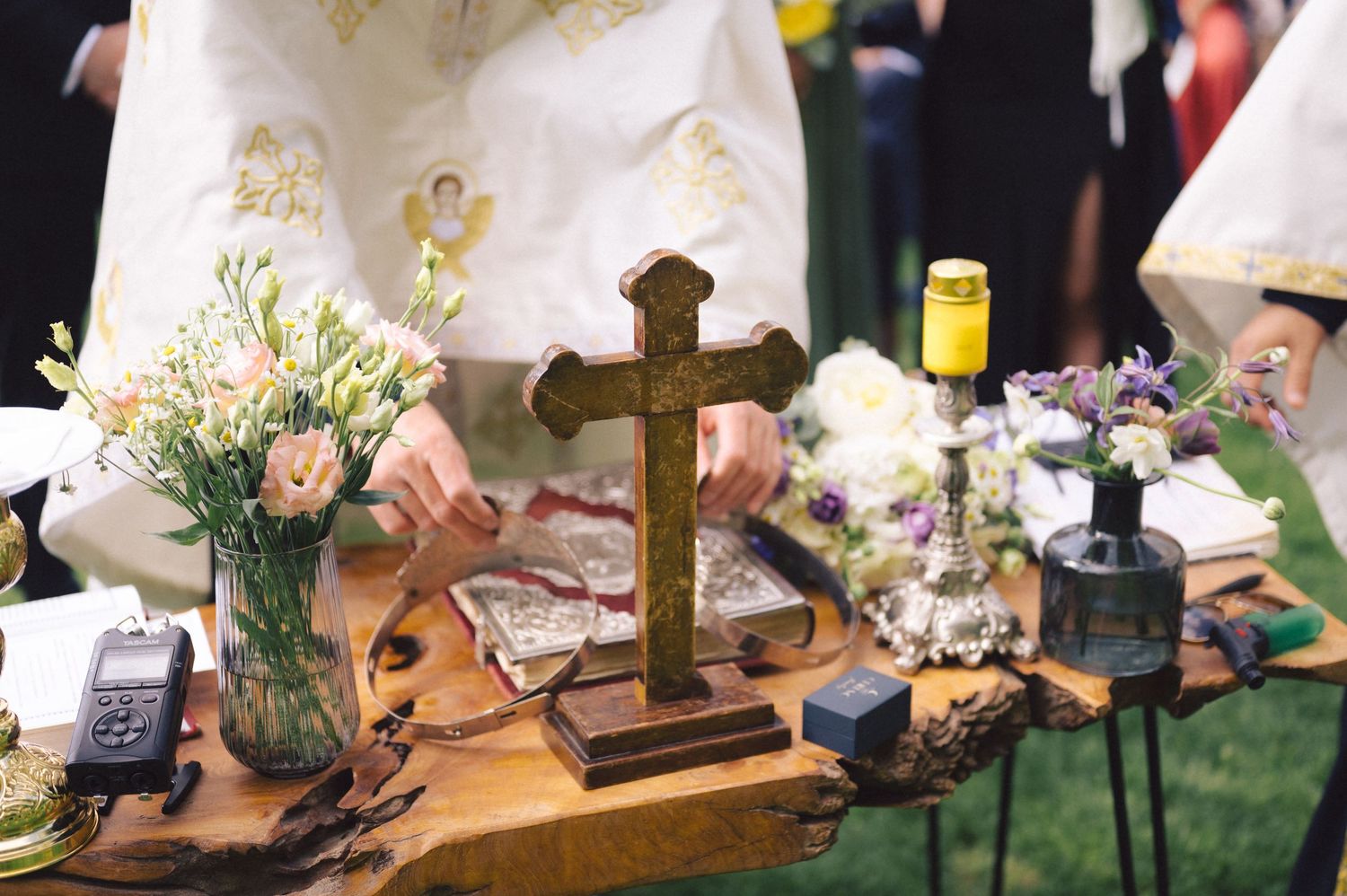 Wooden cross and floral decorations arranged on rustic table at outdoor wedding ceremony setup.