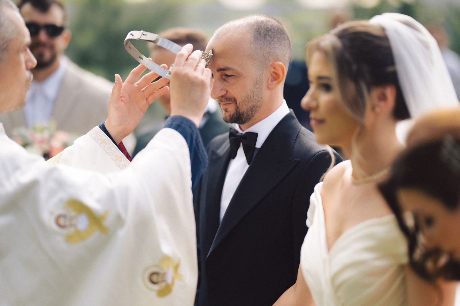A wedding ceremony taking place outdoors with participants standing together during a traditional religious blessing.