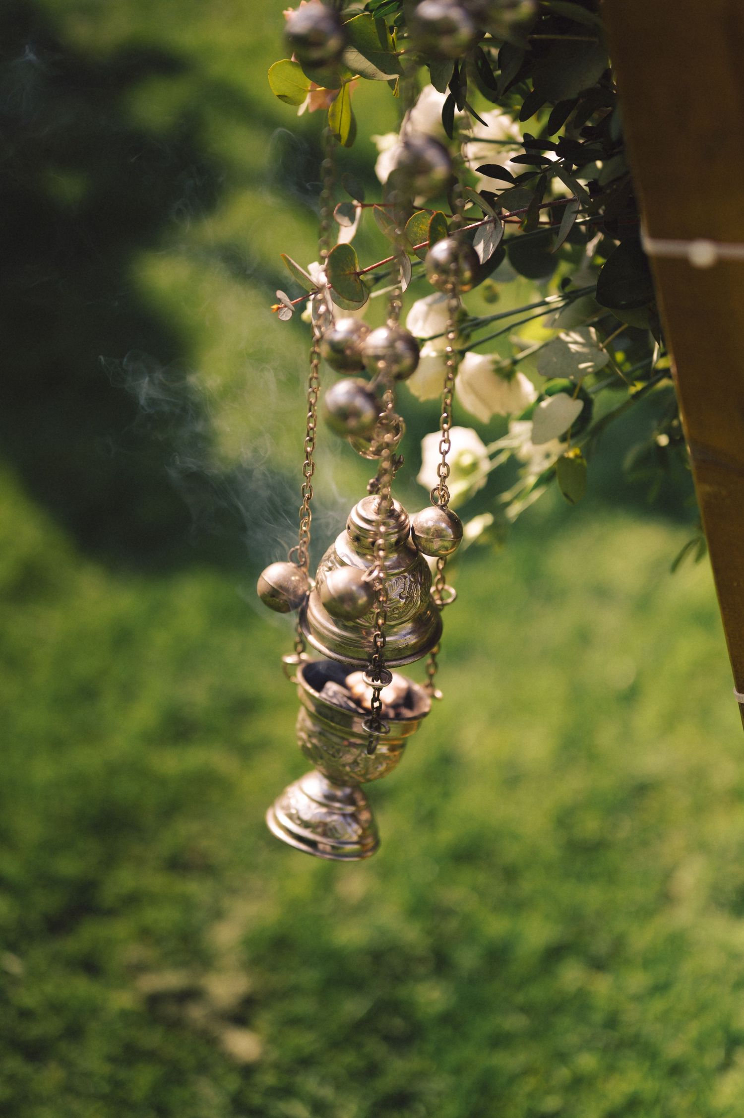 Antique silver incense burner hanging from a chain with blurred green garden background.