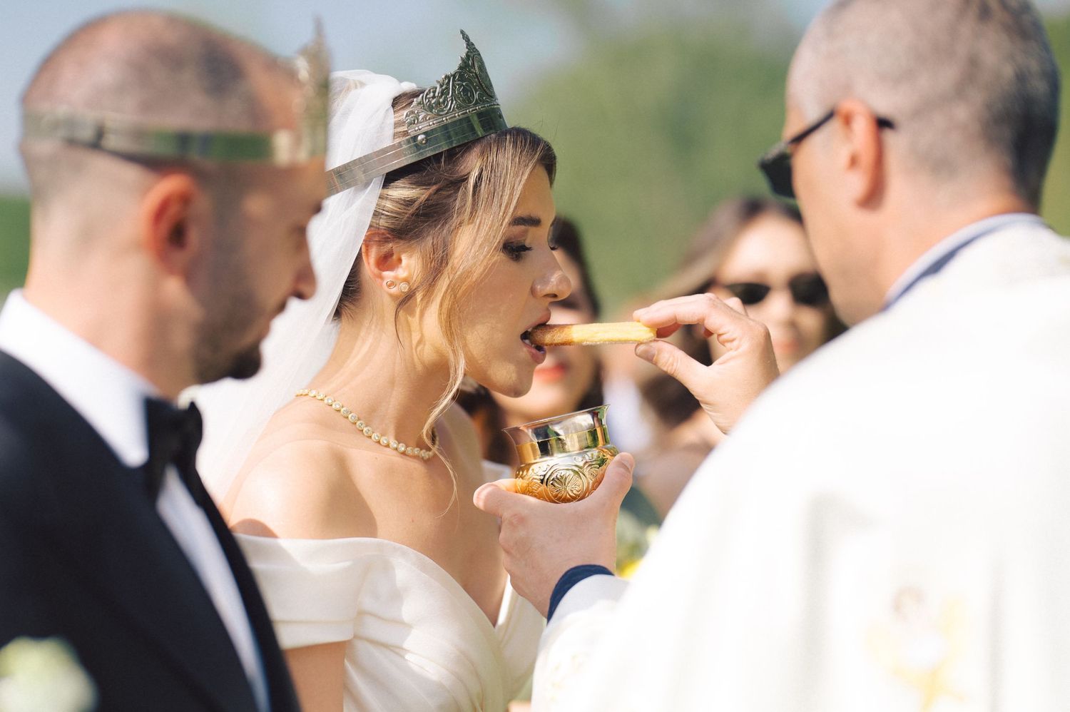 A candid moment at an outdoor wedding ceremony showing a bite of food being shared during the celebration.