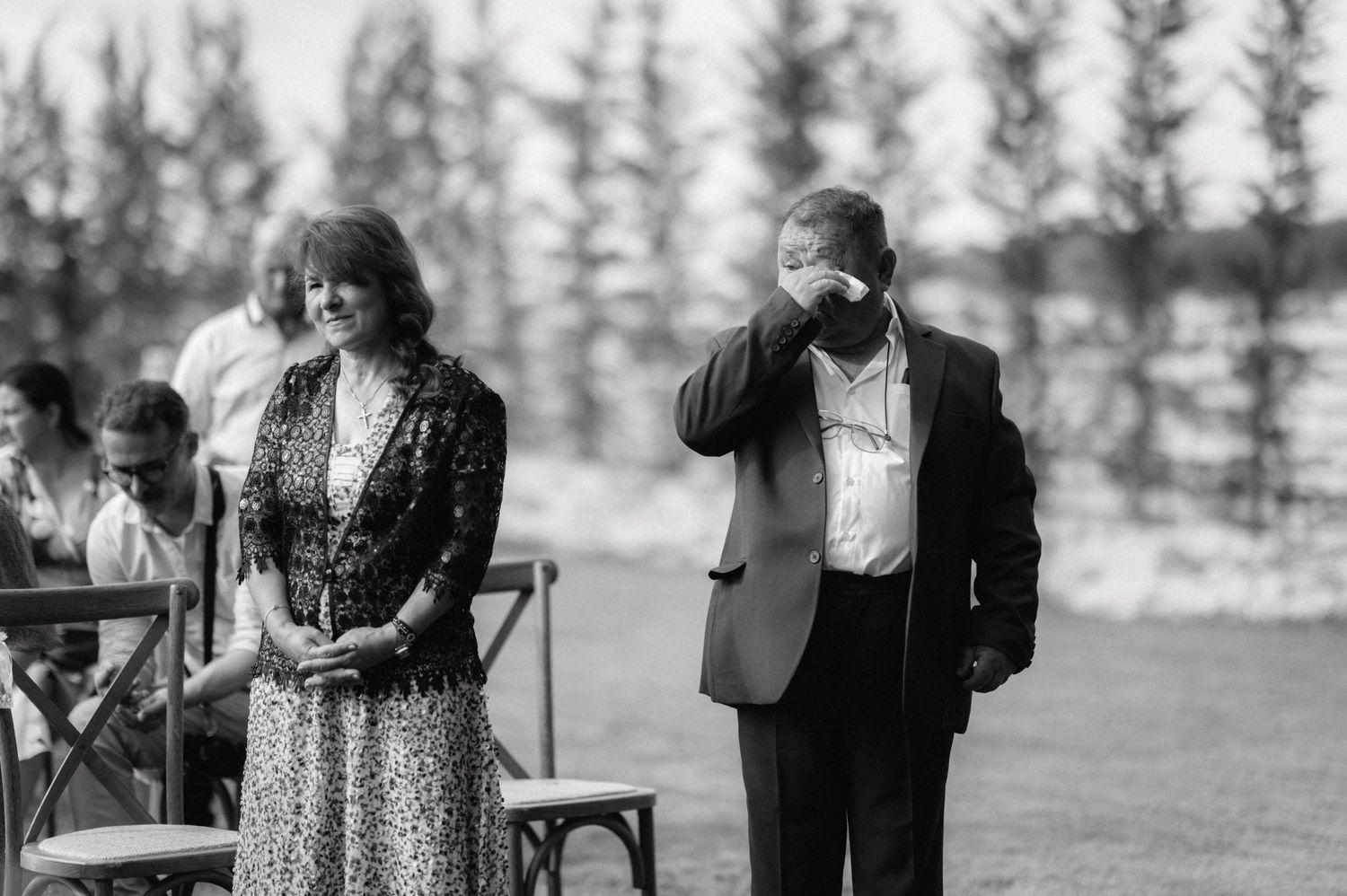 A vintage black and white photograph showing two people outdoors in formal attire at what appears to be a gathering.