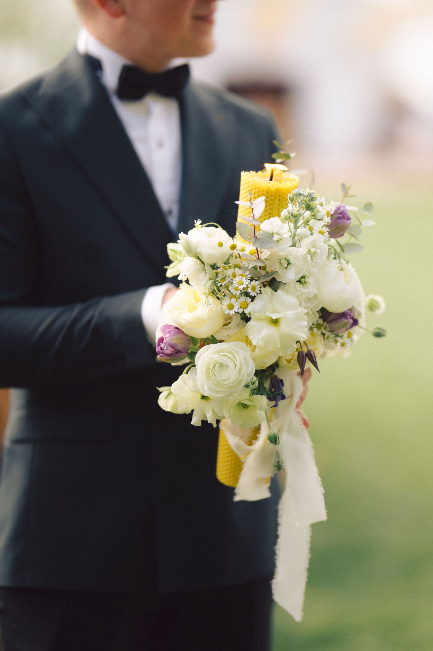 A formal black tuxedo holding an elegant wedding bouquet with white roses, yellow flowers and trailing ribbons.