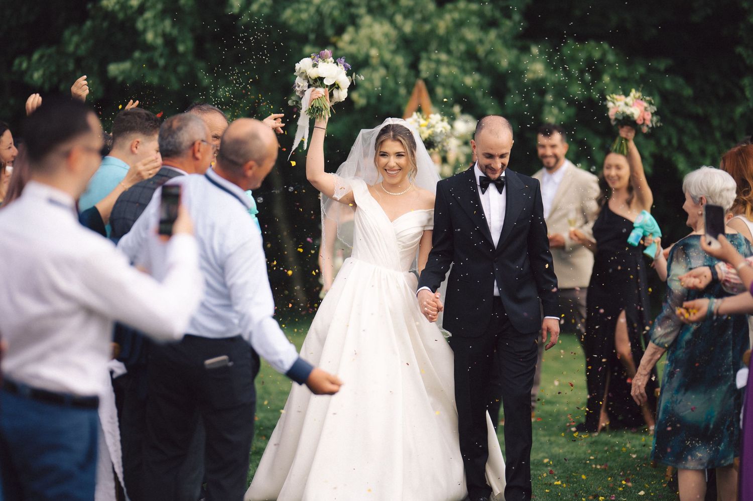 Wedding couple walks down garden path as guests form joyful receiving line to celebrate.
