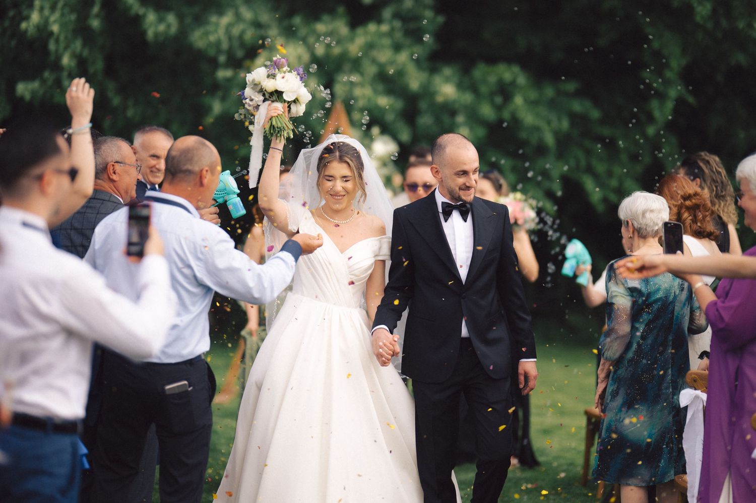 A joyful newlywed couple celebrates with guests during an outdoor garden wedding ceremony.