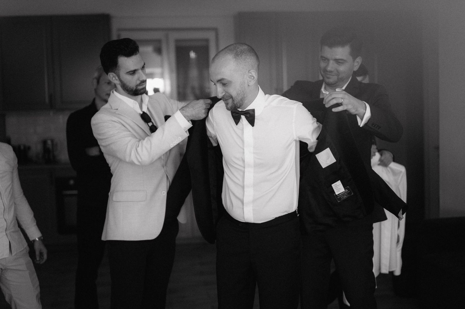 Two men in formal wear playfully attempt to box or spar while another person watches and laughs in the background.