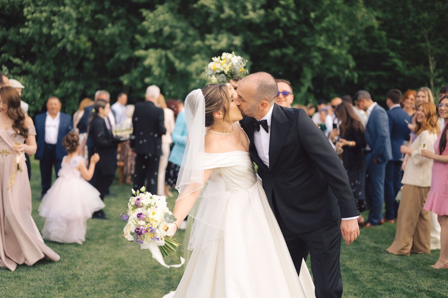 A romantic outdoor wedding ceremony in a garden setting with guests gathered on a lush green lawn.