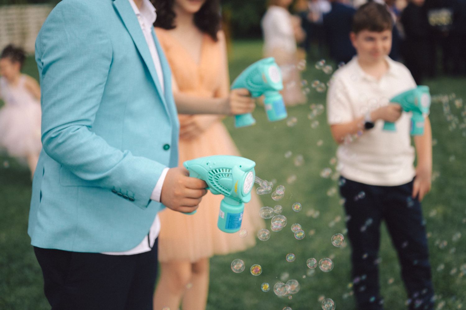 People holding turquoise bubble guns create a magical outdoor scene with bubbles floating through the air.