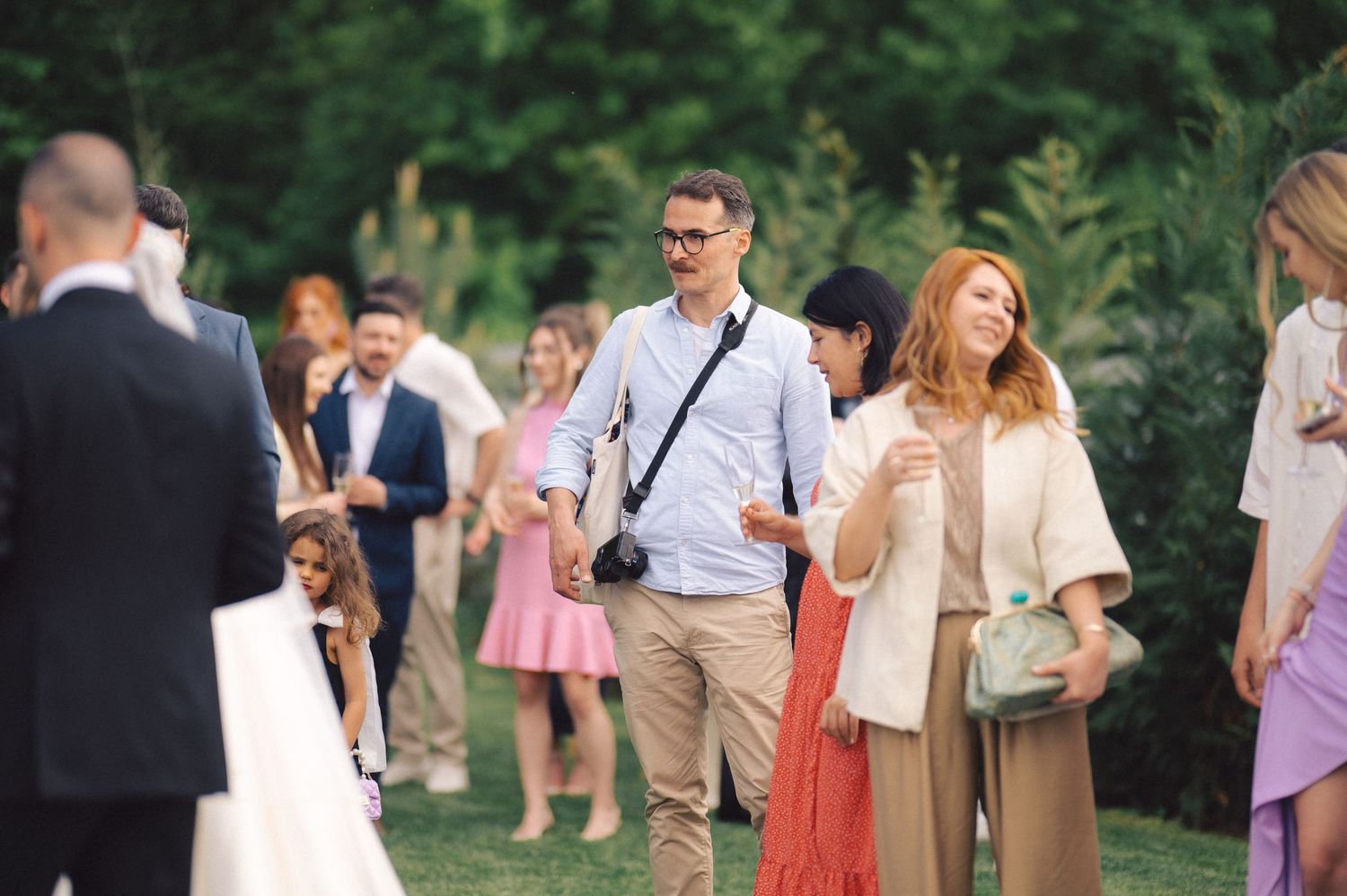 Guests mingle at an outdoor wedding reception in a garden setting during a summer afternoon.