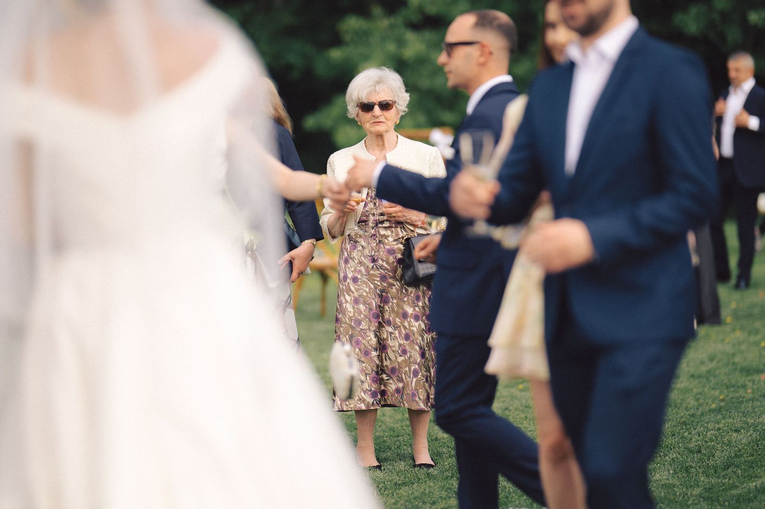 Wedding guests mingle on a grassy lawn during an outdoor reception celebration.