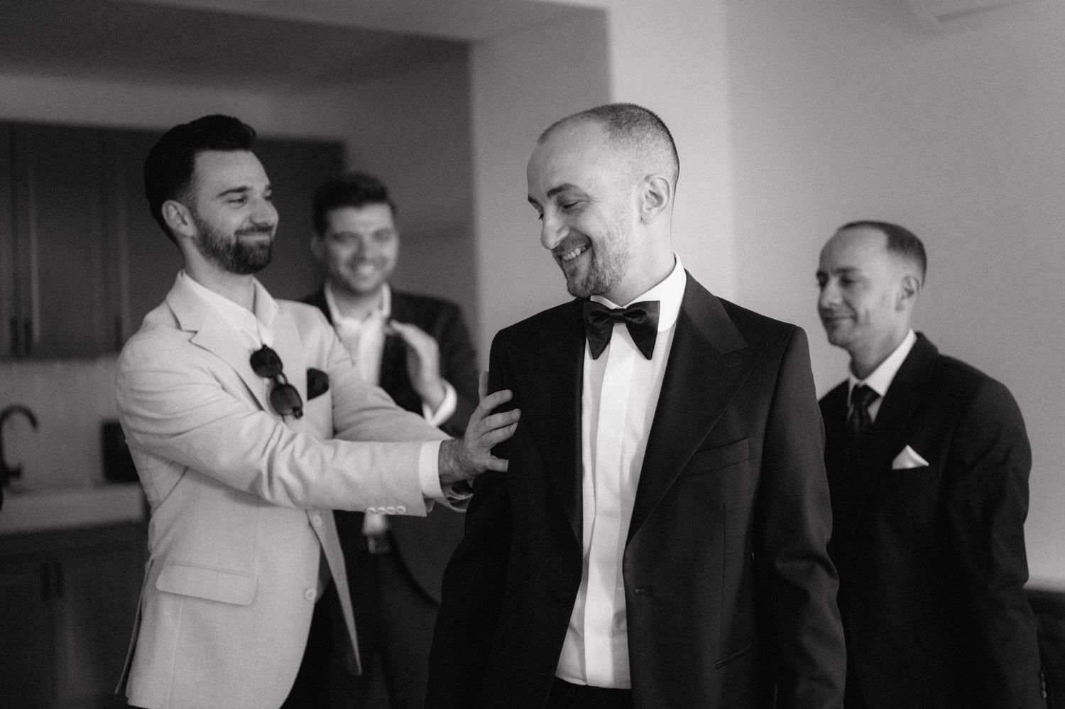 Elegant black and white photograph of groomsmen sharing a lighthearted moment while getting ready in formal attire.