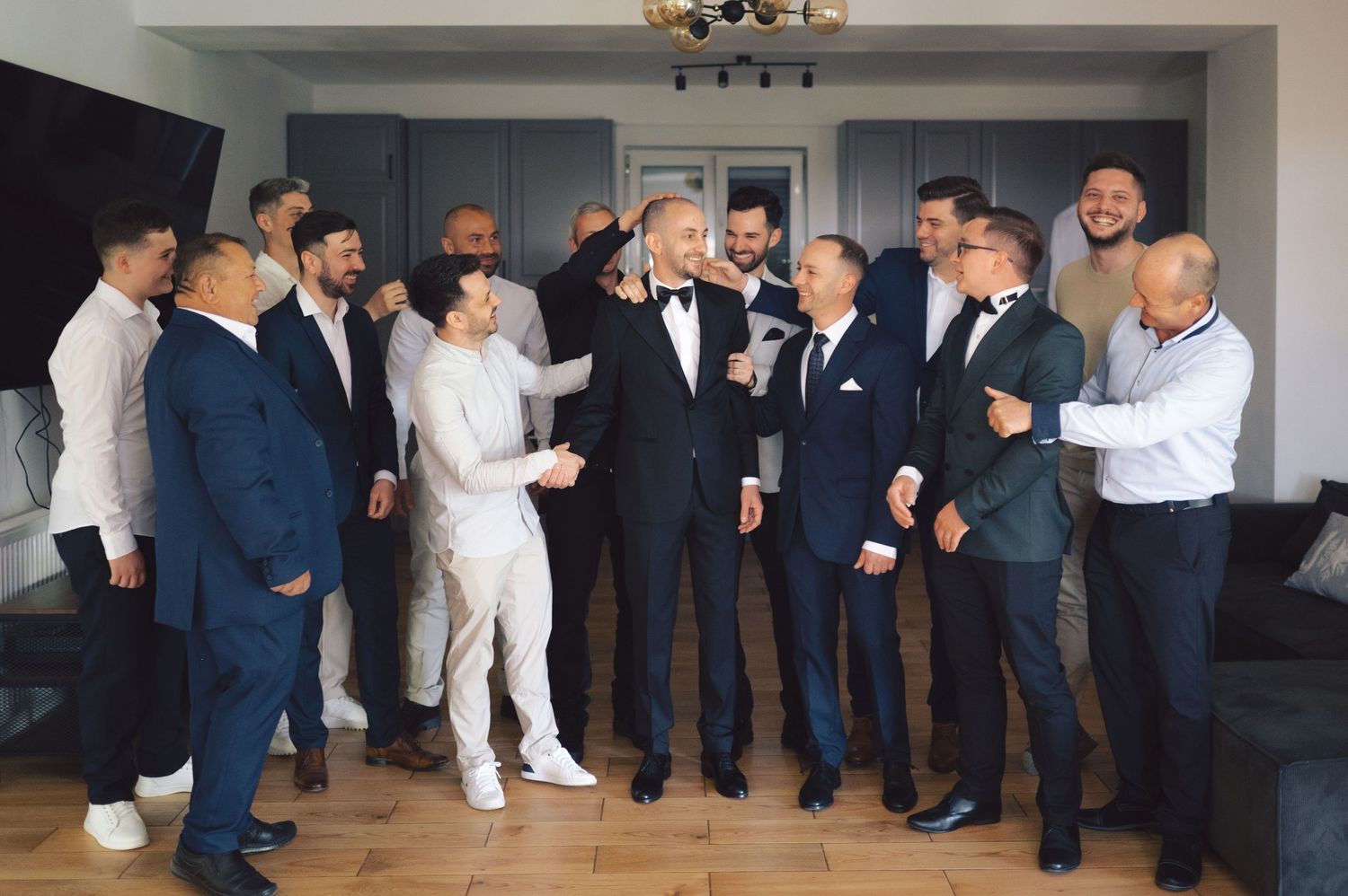 A group of people in formal attire gather in a room, sharing a joyful moment with drinks and laughter.