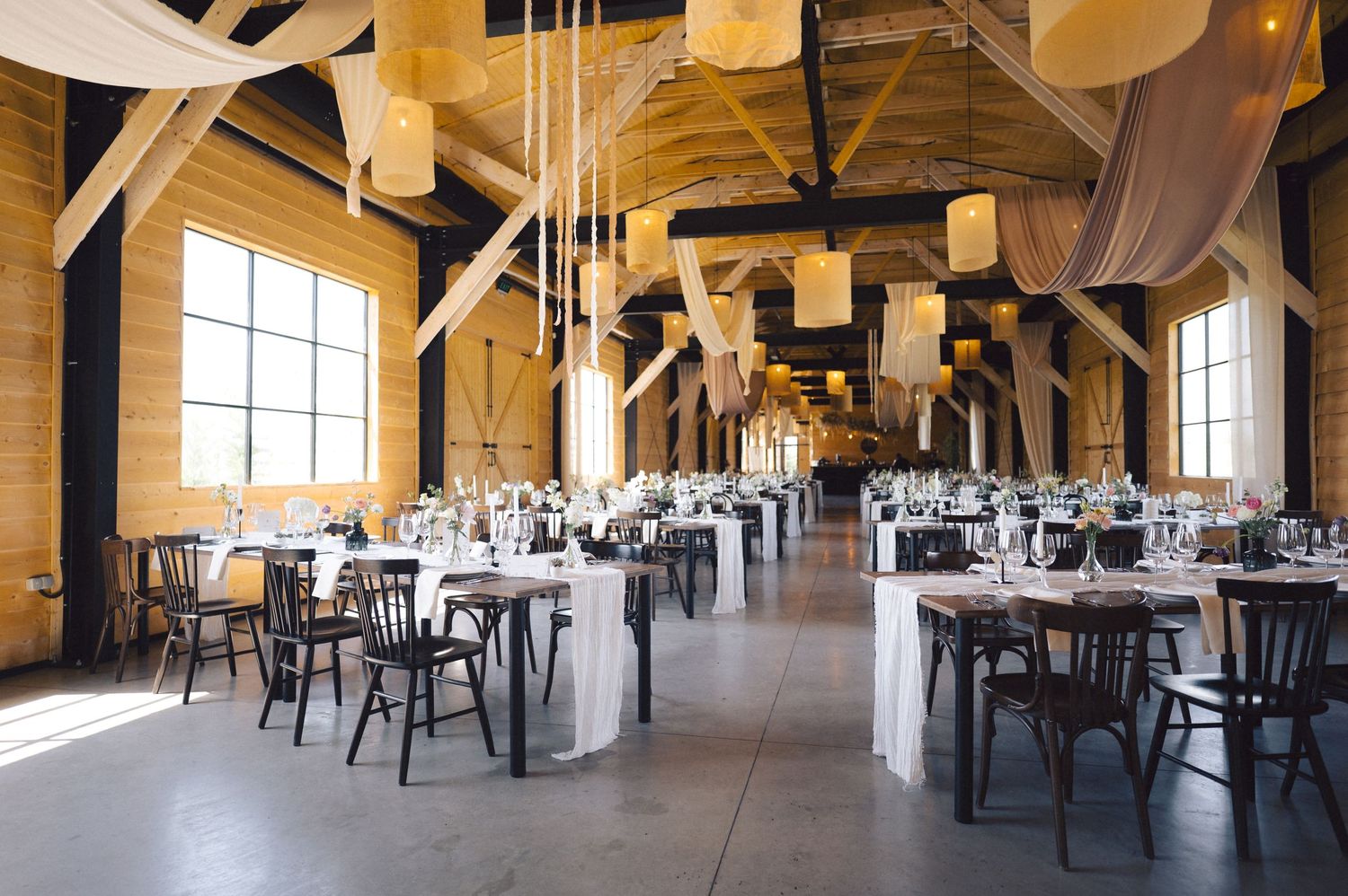 Rustic wedding reception venue with high wooden beams and flowing fabric drapes creating an elegant atmosphere.
