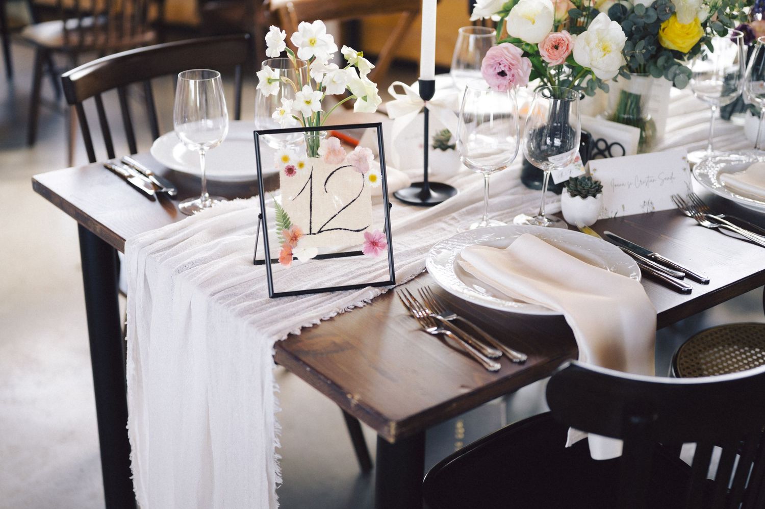 Elegant tablescape with white linens, floral centerpieces, wine glasses and black chairs at a formal event.