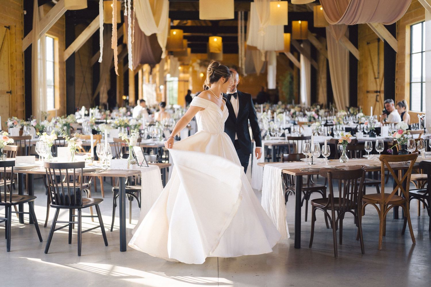 A rustic wedding reception venue with wooden beams and cross-back chairs arranged for a celebration.
