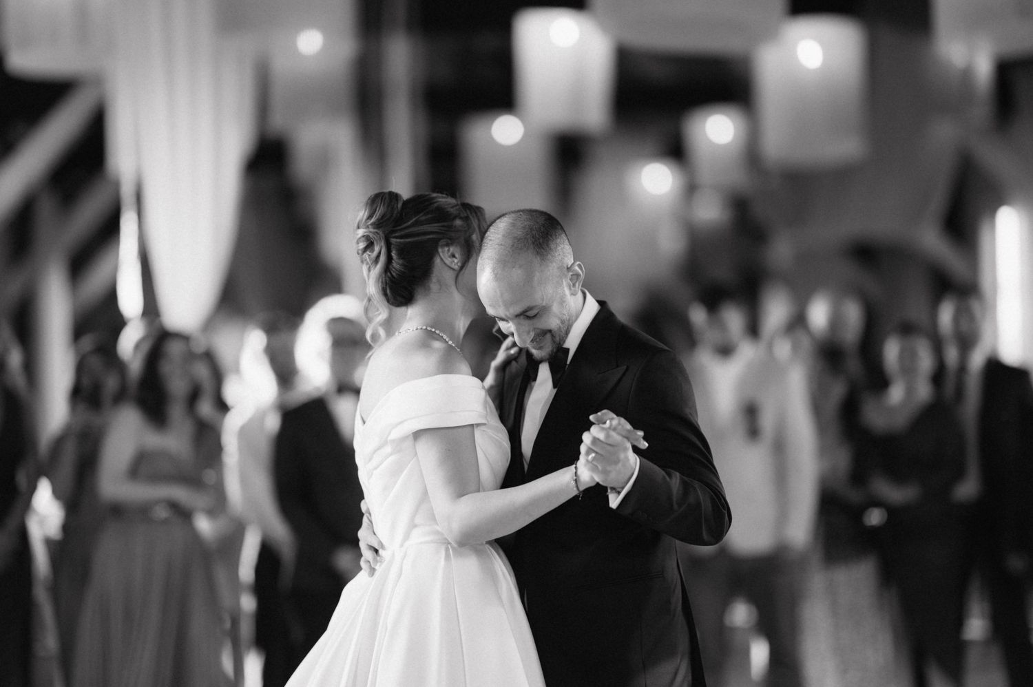 A romantic black and white photograph of a wedding couple's first dance under soft lighting at their reception.