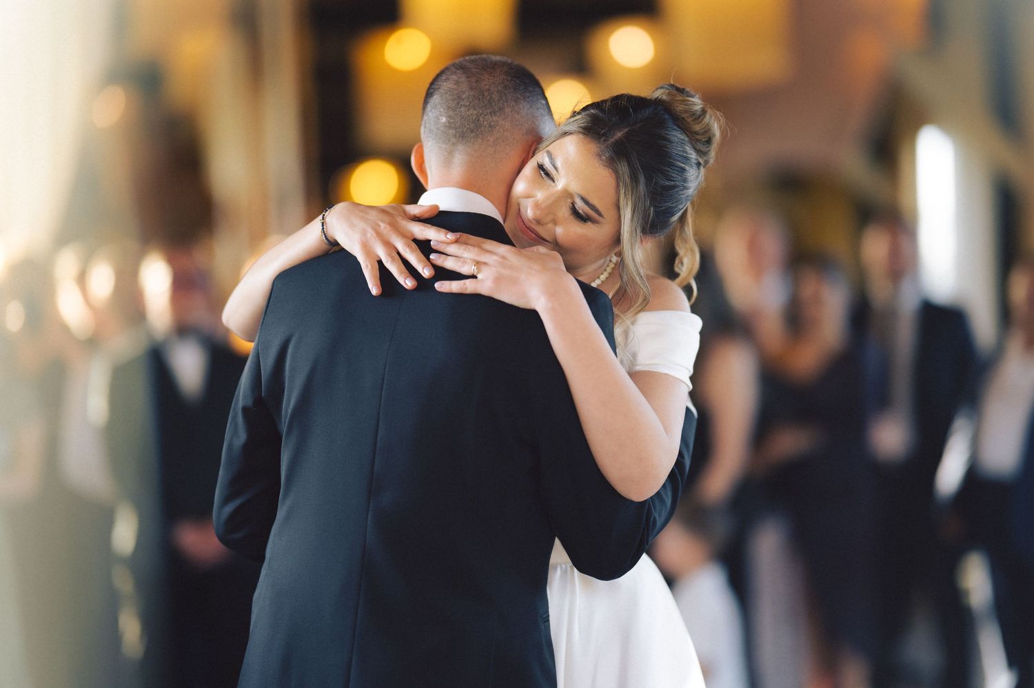 A couple shares a tender embrace during their first dance at an elegant indoor wedding reception.
