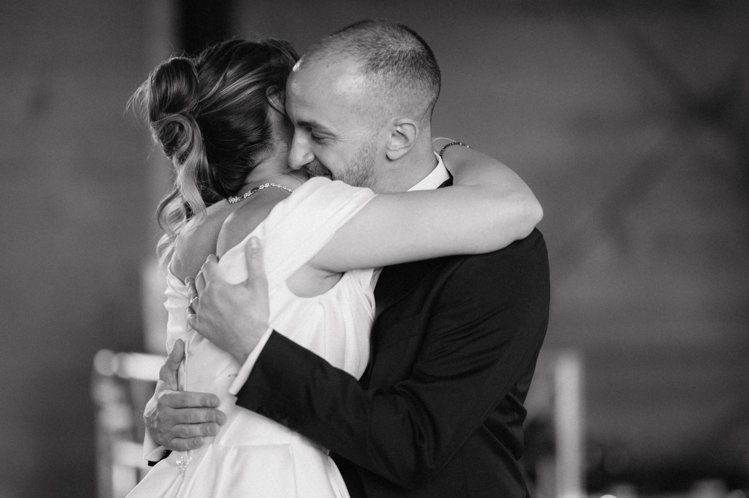 A tender black and white photograph captures an intimate moment between a couple embracing at their wedding.