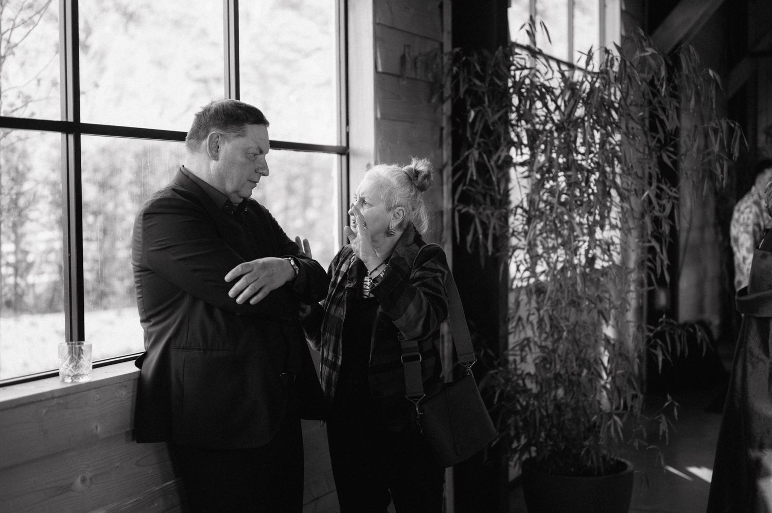 Two figures engage in intimate conversation beside a bright window in a black and white vintage photograph.