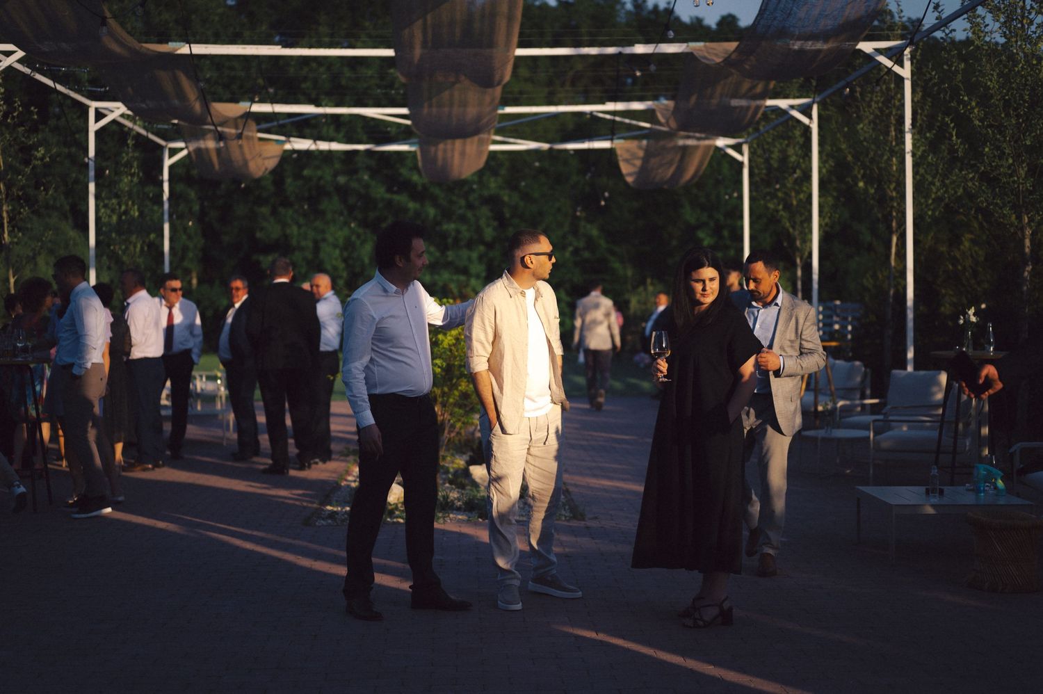 People walking under mounted lighting fixtures at dusk in an outdoor urban setting.