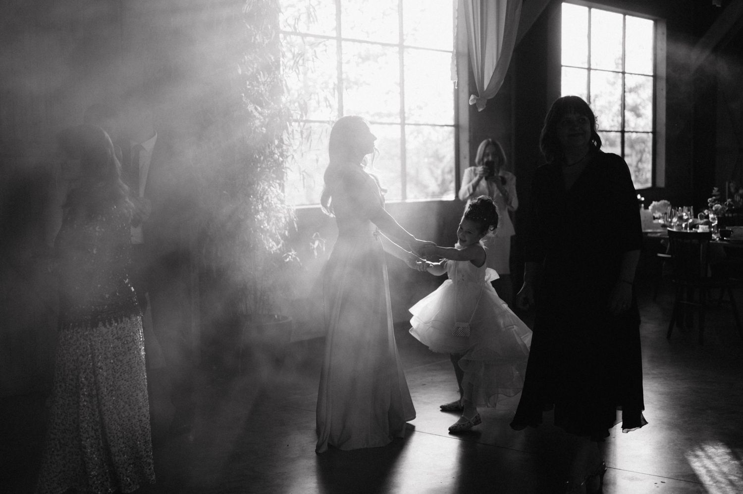 Silhouettes dance in atmospheric hazy light streaming through windows during an elegant event.