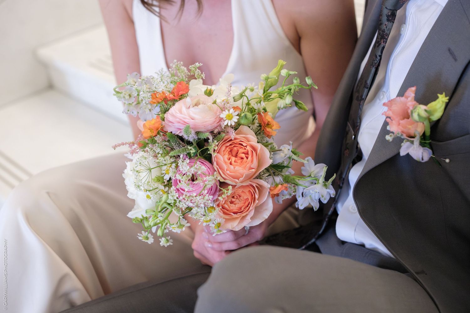 Close up of pastel peach and pink wedding bouquet held between bride and groom on marble steps.
